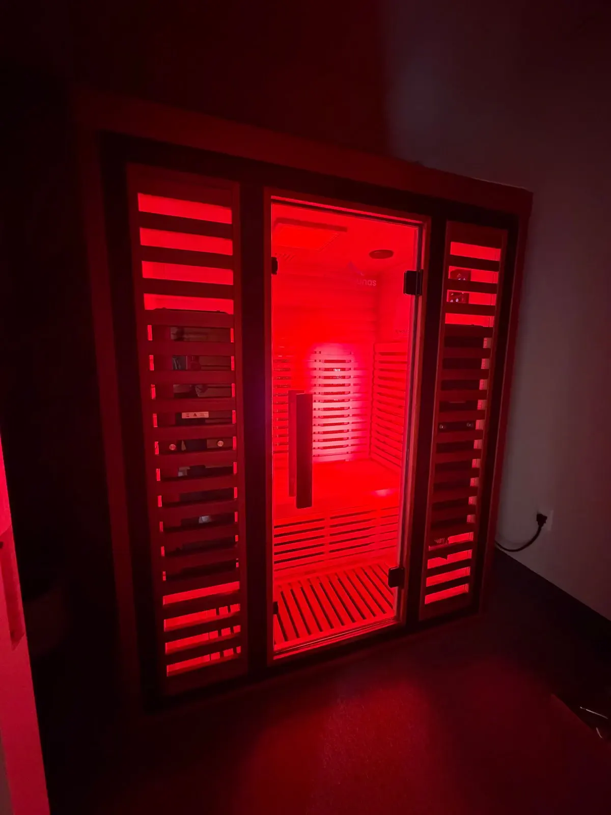 Wooden infrared sauna cabin with glass door and red light therapy panels lit inside